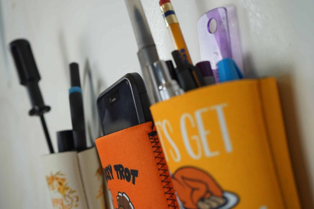 Custom koozies holding pencils and a phone