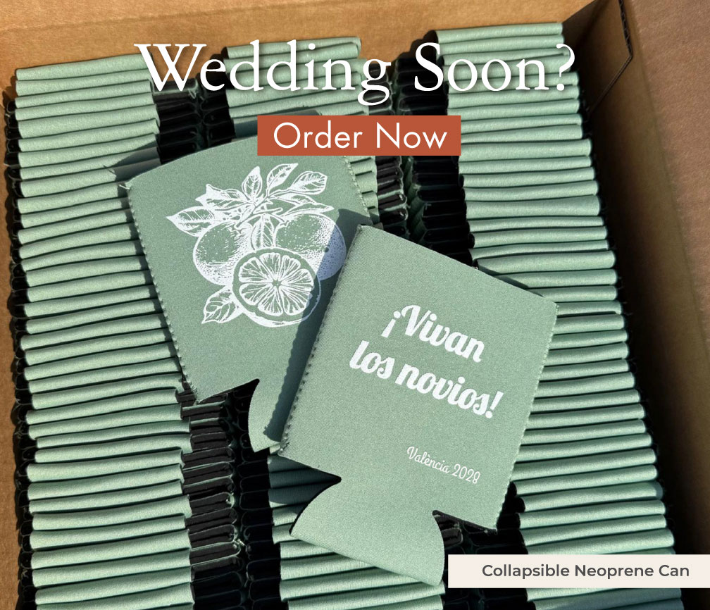 Sage green collapsible neoprene can coolers on cans at a rustic wedding table, white citrus print and ¡Vivan los novios!, custom wedding coolies beside wildflowers and a wooden wedding sign.