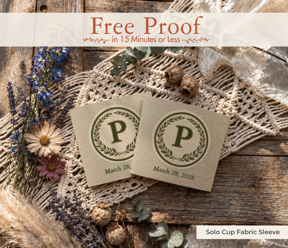 Two kraft fabric solo cup sleeves with a laurel wreath monogram P and wedding date, styled on wood with lace, dried flowers, and pampas as a custom wedding favor.